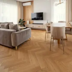 Eleganckie wnętrze z szarą kanapą i jadalnią. Wzrok przyciąga piękna podłogówka ułożona we wzór jodełki.