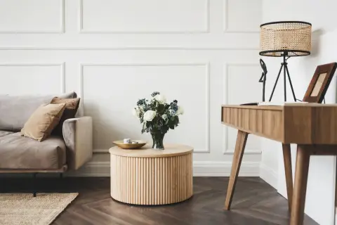 Elegancki salon w stylu klasycznym: beżowa sofa, drewniany stolik z bukietem róż, biurko i lampa z wiklinowym kloszem.